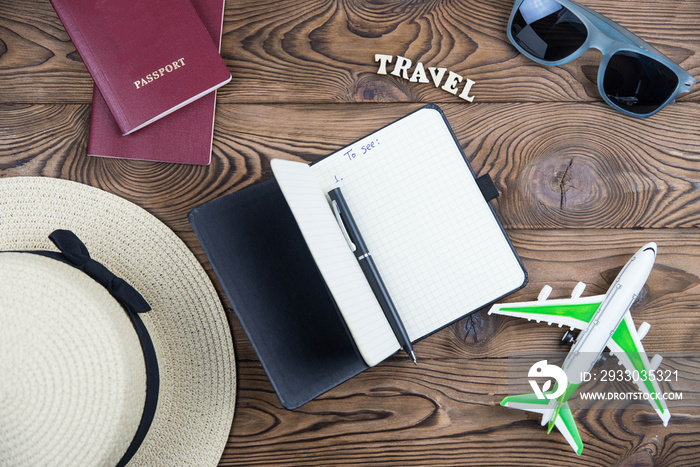 Flat lay traveler accessories on wooden background with straw hat, passport, airplane, and sunglasses.  Top view travel and planning summer vacation concept.