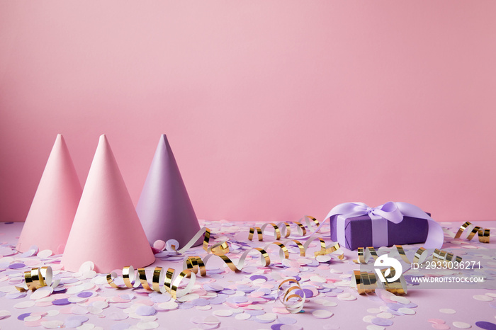 party hats, gift box and confetti pieces on violet tabletop