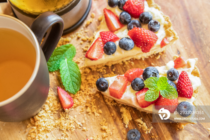 piece of strawberry and blueberry cheescake on plate and cup of tea served for breakfast at home, hotel or cafe. Dessert meal, sweet food . High quality photo