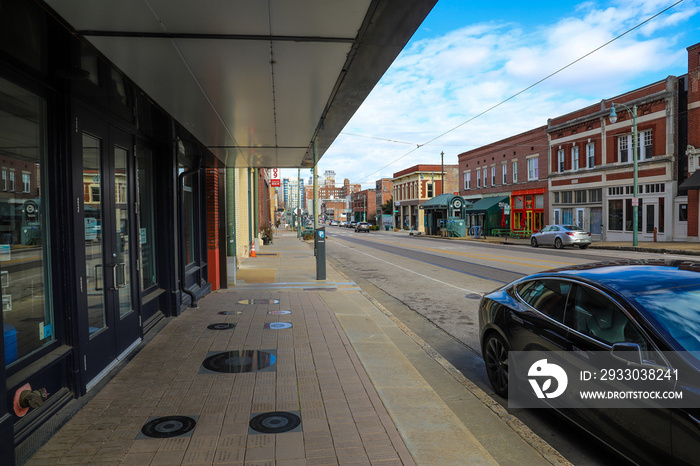 a long street with a yellow line in the center filled with parked cars and office buildings and skyscrapers along the street with blue sky and clouds in Memphis Tennessee USA