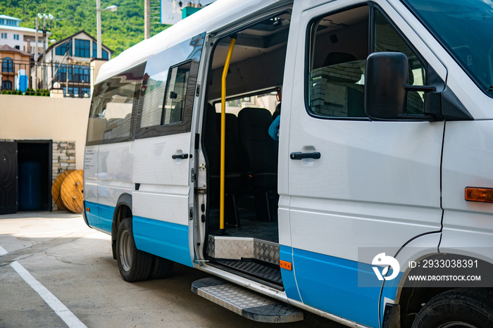 Tourist minibus is waiting with the door open in the parking lot. White minibus is parked in sunny weather.