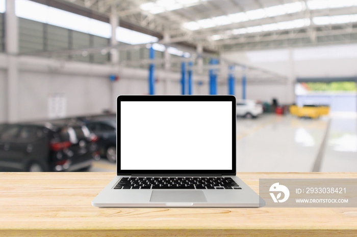 Laptop computer on wood table with car service centre with auto at repair station bokeh light defocused blur background