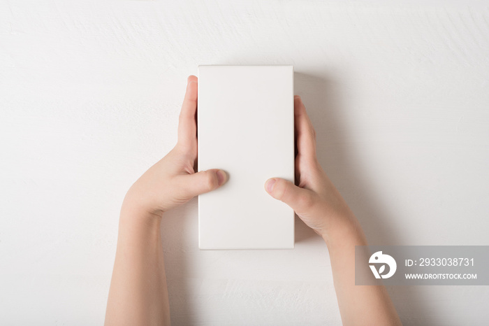 White rectangular cardboard box in children’s hands. Top view, white background