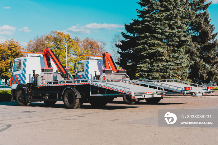 Two new tow trucks parked near the road in the city. Cranes on truck to towing cars. Urban. Service. Side view. Tows with lifters