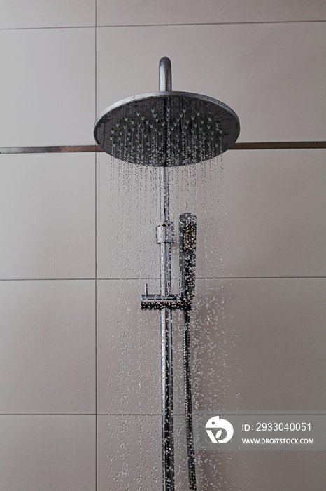 Shower with a tiled background in the bathroom. Water flies from chrome showers in drops. Bathroom fittings as an element of equipment and a modern design at home.