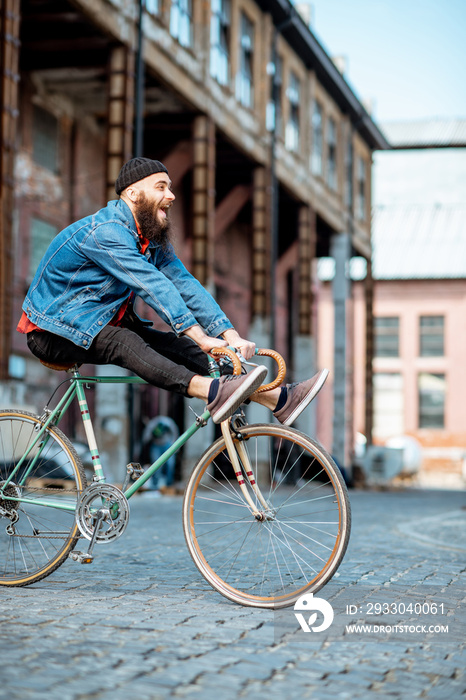 Stylish man as a crazy hipster having fun, riding retro bicycle outdoors on the industrial urban background