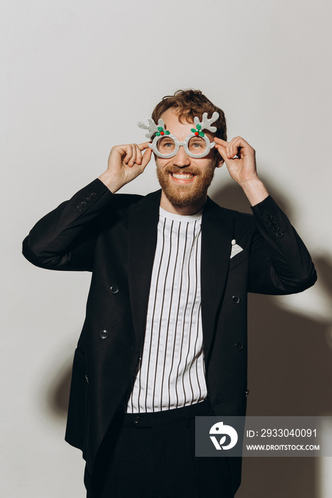 Young man in black jacket with party glasses on color background.