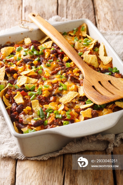 Traditional frito pie with ground beef, cheese, corn, beans and chips close-up in a baking dish. vertical