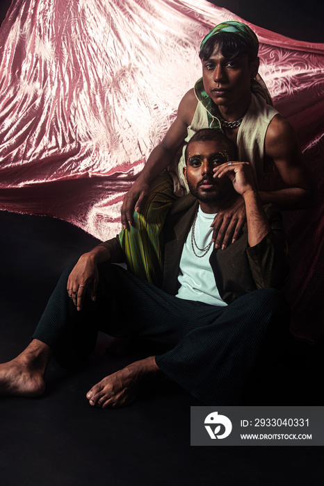 Two Malaysian Indian men in a studio setting with cloth flying in the background, posing against a black bacground