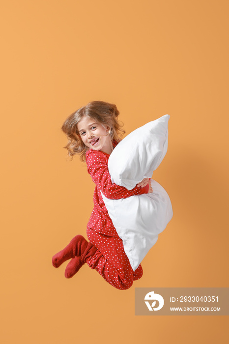 Jumping little girl in pajamas and with pillow on color background