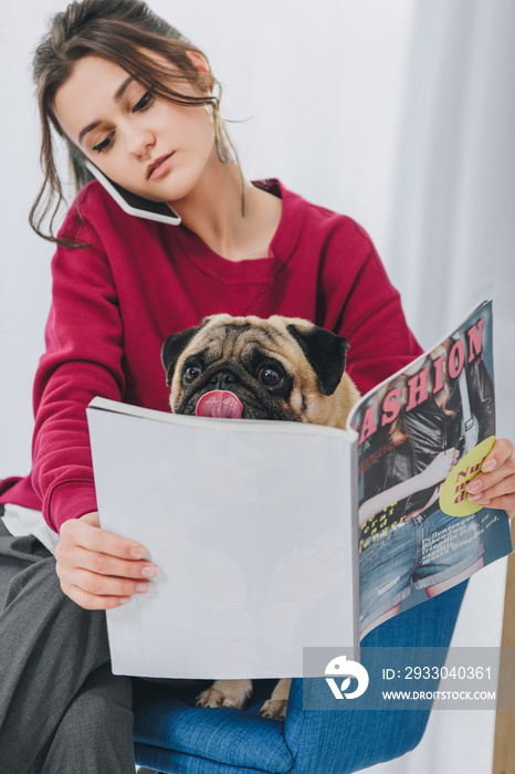 Attractive young girl talking on the phone and hugging pug dog