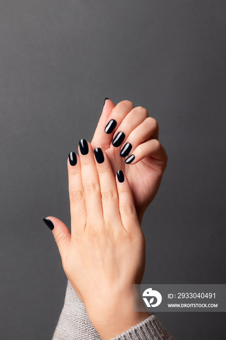 Female hands with beautiful manicure - dark black nails on gray background. Nail care concept