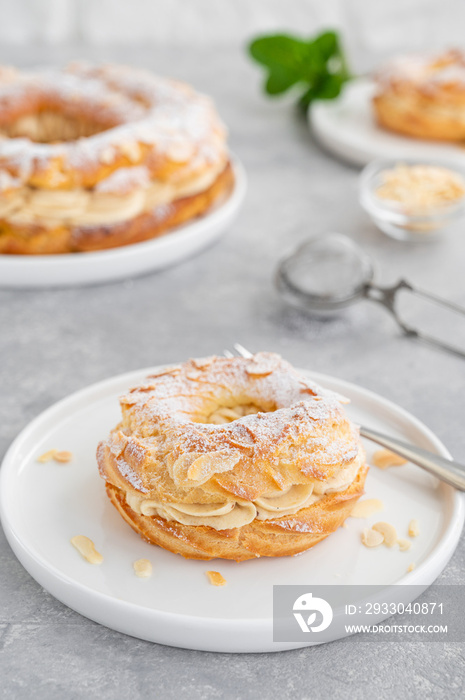 French traditional cake Paris Brest with praline cream, powdered sugar and almond petals on top on a gray concrete background. Copy space.