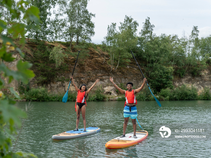 Friends standing with arms raised on paddleboards on lake