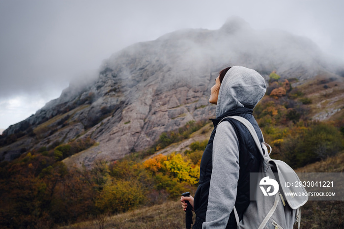 Asian travel woman stands by the mountain. Cold weather, fog on the hills. Autumn hike. The beginning of the autumn season. Beautiful foggy weather