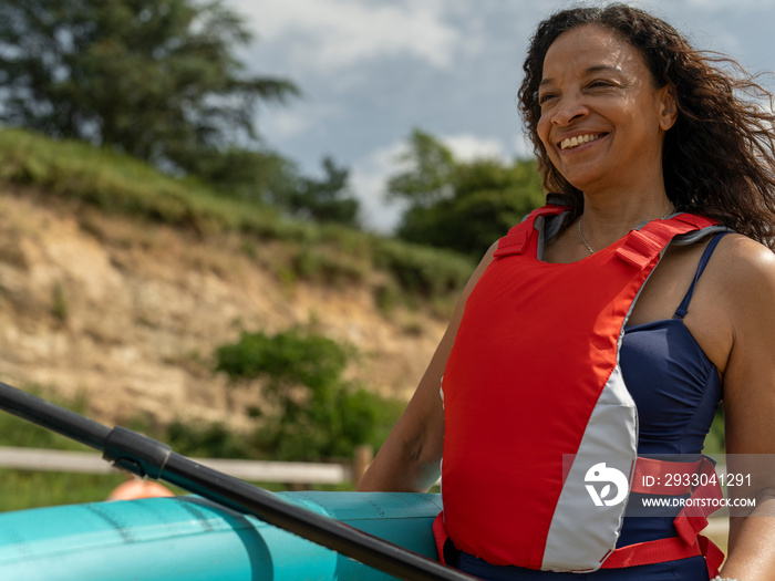 Portrait of smiling woman carrying paddleboard and oar on beach