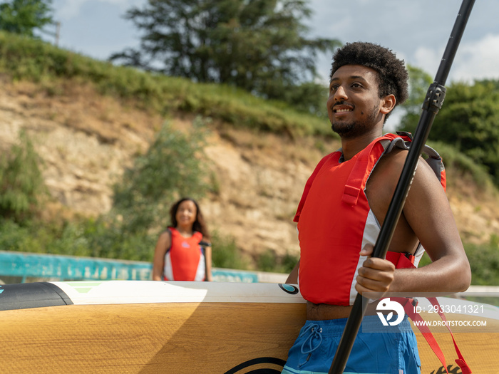 Woman looking at man carrying paddleboard and oar