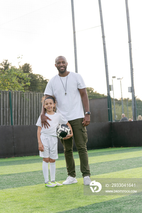 Portrait of man and girl (6-7) with ball on soccer field