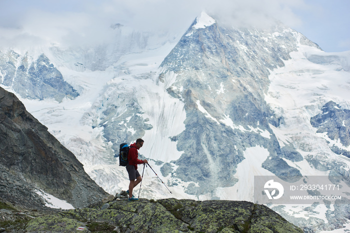 Horizontal snapshot of amazing, rocky mount Ober Gabelhorn in snow in the Pennine Alps in Switzerland, located between Zermatt and Zinal, traveller walking with trekking poles on foreground