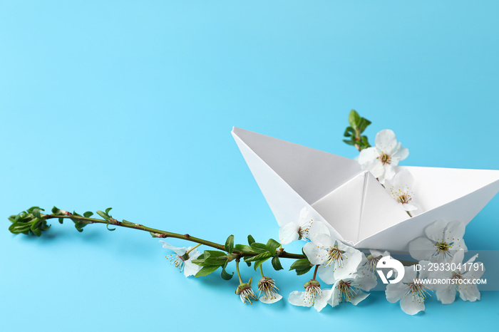 Beautiful blooming spring branch and origami boat on blue background