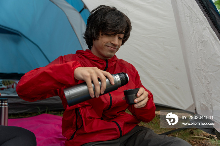 Young man drinking from insulated drink container while camping