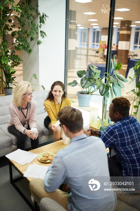 Two women and two men in casualwear sitting by table in office while working with papers at meeting