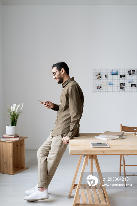 Young business employee in casualwear scrolling in smartphone by workplace