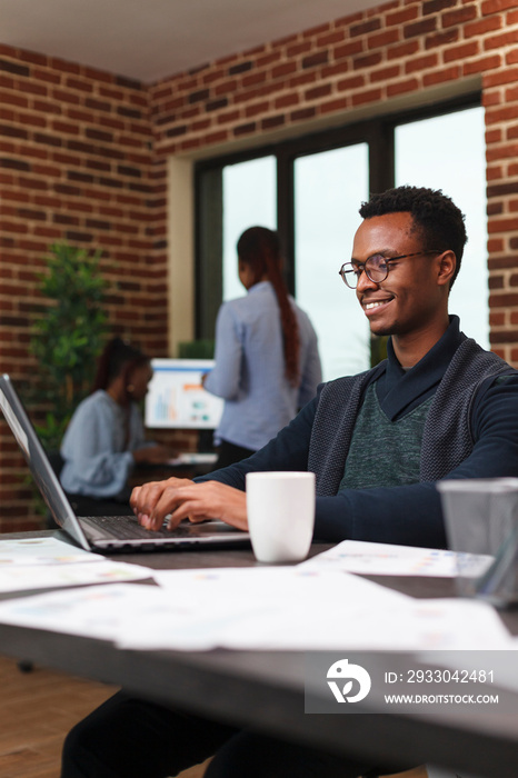 Smiling african american business man developing startup marketing strategy and advertisement plan. Company office employee working on financial graph data while using work computer laptop.