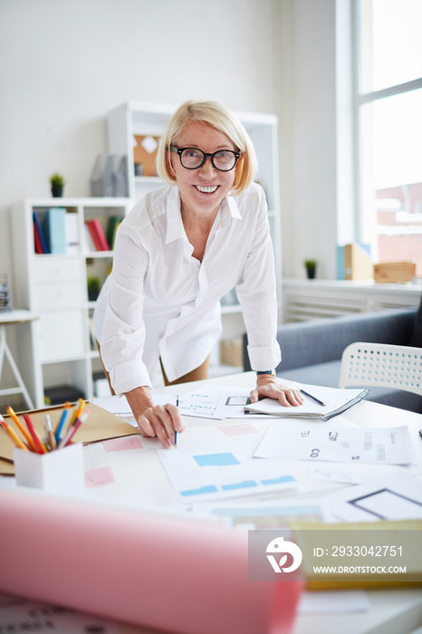 Portrait of smiling mature woman looking at camera while working with designs in modern print shop