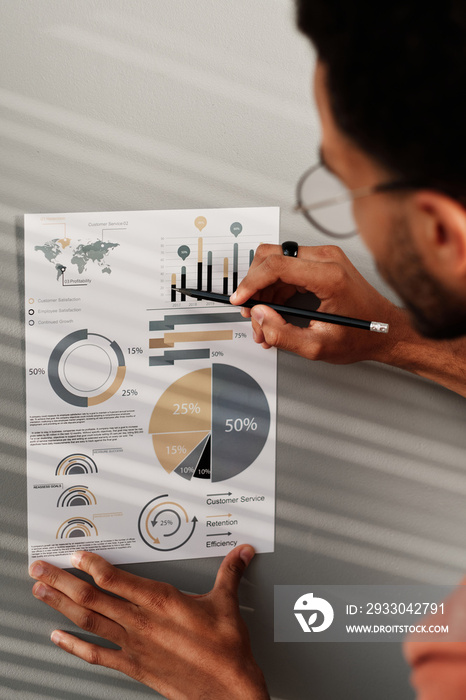 Over shoulder view of marketing specialist drawing with pencil on chart while working with statistics