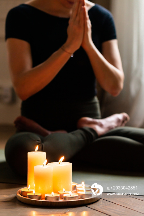 Close-up. Woman in yoga lotus pose meditating in a dark room with candle light. Atmosphere of relax and zen. Exercise to reach clarity of mind and perfect body. Wooden floor, soft morning light