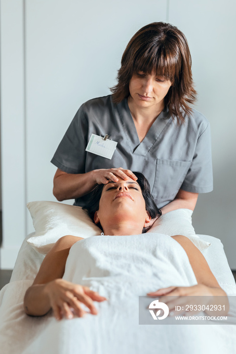 Young physiotherapist doing a neck and face treatment while having reiki healing to the patient in a physiotherapy room.