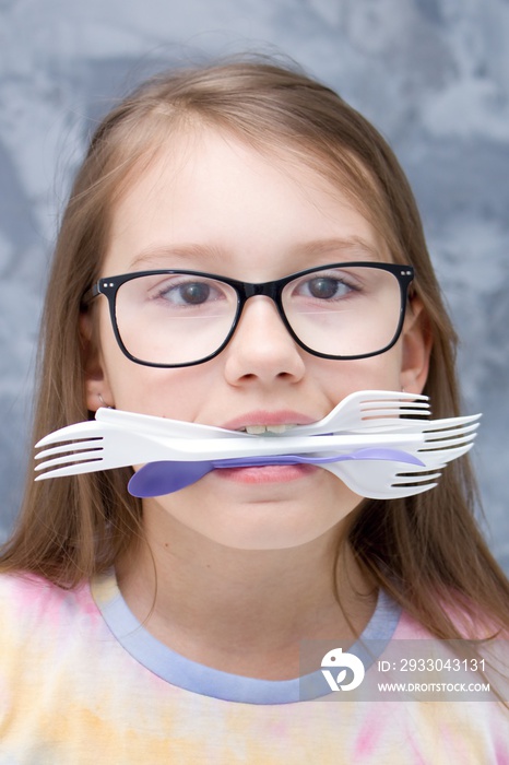 The girl has plastic cutlery and spoons in her teeth. Let`s protect the planet from disposable plastic.