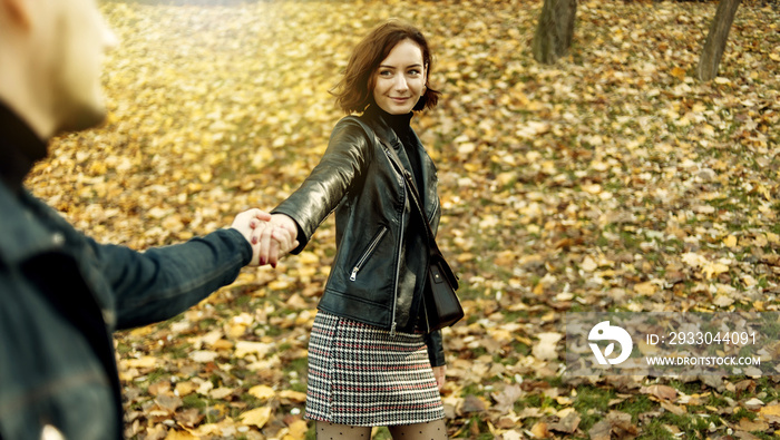 Romantic date. A young couple of lovers fooling around holding hands on the background of fallen autumn leaves. Follow me