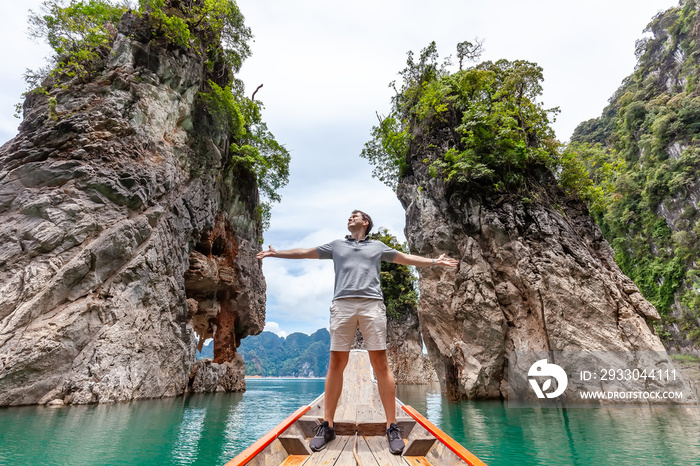 Happy Young Tourist Man at Longtail Boat near Famous Three rocks with Limestone Cliffs at Cheow Lan Lake. Male on Holiday Travel Tour Spreading Arms to Side in Khao Sok National Park in Thailand