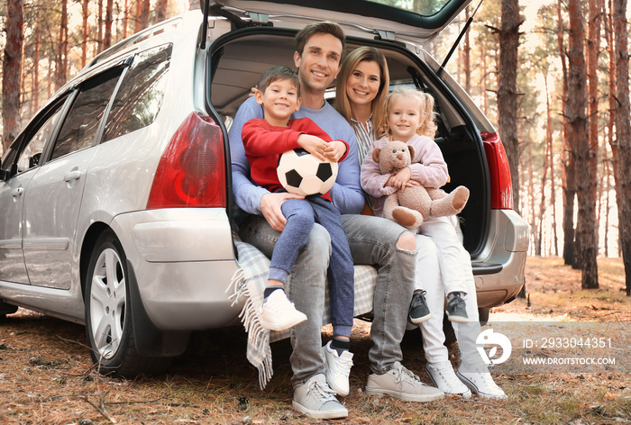 Young couple with their little children sitting in car trunk