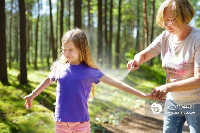 Middle age woman applying insect repellent to her granddaughter before forest hike beautiful summer day. Protecting children from biting insects at summer.