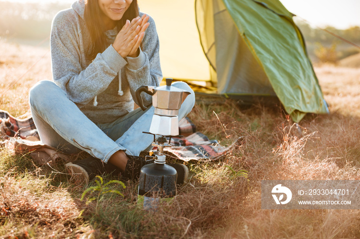 Young woman making coffee outdoors near a tent