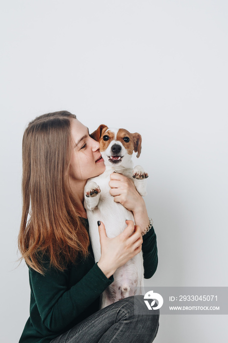 Cute young woman kisses and hugs her puppy jack russell terrier dog. Love between owner and dog. Isolated on white background. Studio portrait.