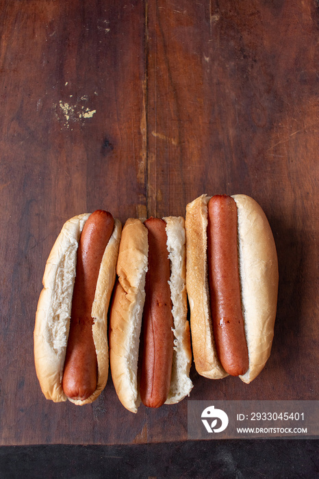 row of plain hot dogs in buns flat lay on wood table