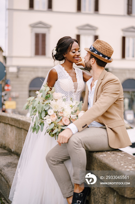 Wedding in Florence, Italy. Interracial wedding couple. African-American bride in a white dress with a long veil and a bouquet, and Caucasian groom in a sandy jacket and straw hat.