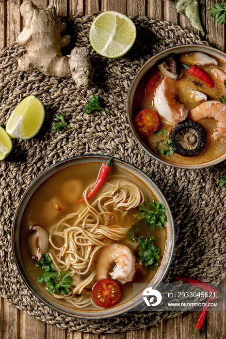 Variety of asian soups. Traditional spicy Thai tom yum kung and noodles soup with shiitake mushrooms, prawns, ingredients above on straw wicker napkin over wooden plank background. Flat lay, space.
