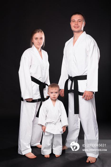 Portrait of happy young family in martial arts uniform standing over black background.