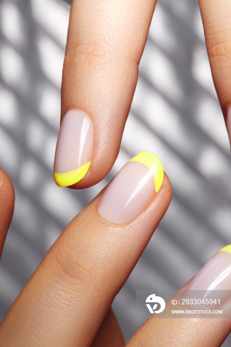 Hands with bright yellow french manicure. Nails art design. Close-up of hands with trendy neon nails on striped print