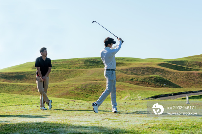 Professional golfer asian two man approach on the tee off for swing and hitting golf ball and looking fairway in course. Hobby in holiday and vacations in sunny morning day on club golf.  Lifestyle