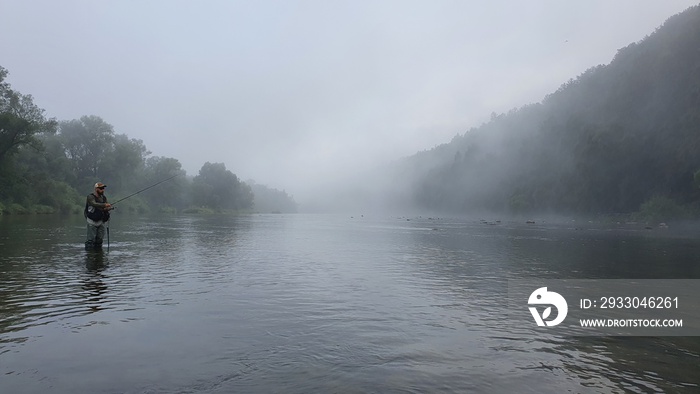 Silhouette of a fisherman, a rod and a breathtaking scene in Bieszczady mountains with fog on San river. Article about fishing day hunting for a trout.