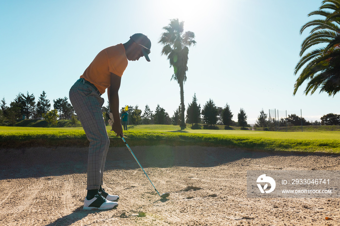 Side view of african american young man with golf club standing against clear sky at golf course