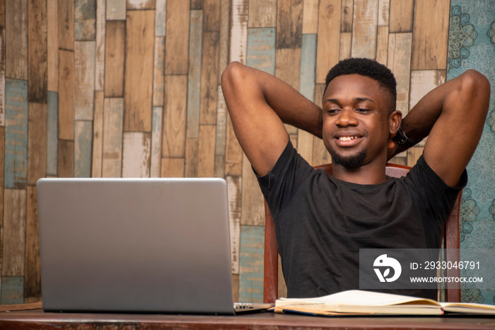 african teenager studying at home using his laptop, receiving lectures online, smiling