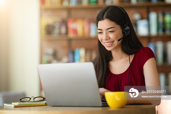 Online Tutoring. Asian Woman Tutor With Headset Working On Laptop In Cafe