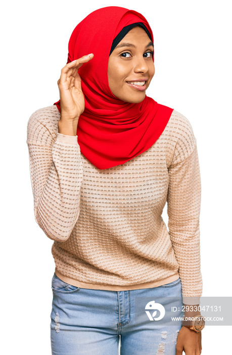 Young african american woman wearing traditional islamic hijab scarf smiling with hand over ear listening an hearing to rumor or gossip. deafness concept.